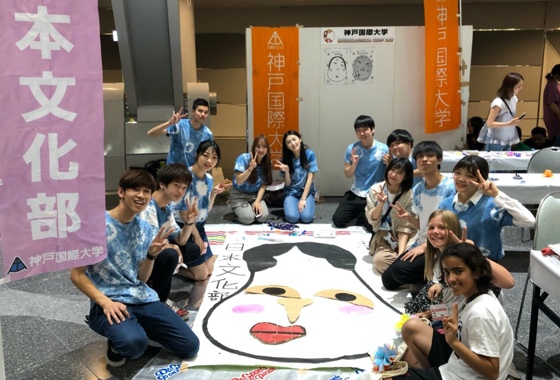 多国籍な大学生たちが床に置いてある大きい絵を囲んでいる
